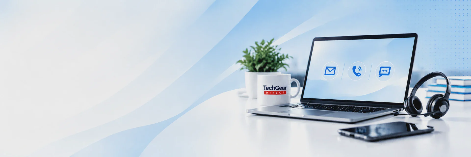 Laptop showing email, phone and chat icons beside a TechGear Direct mug, a small plant, a headset, a smartphone and notebooks on a bright white desk